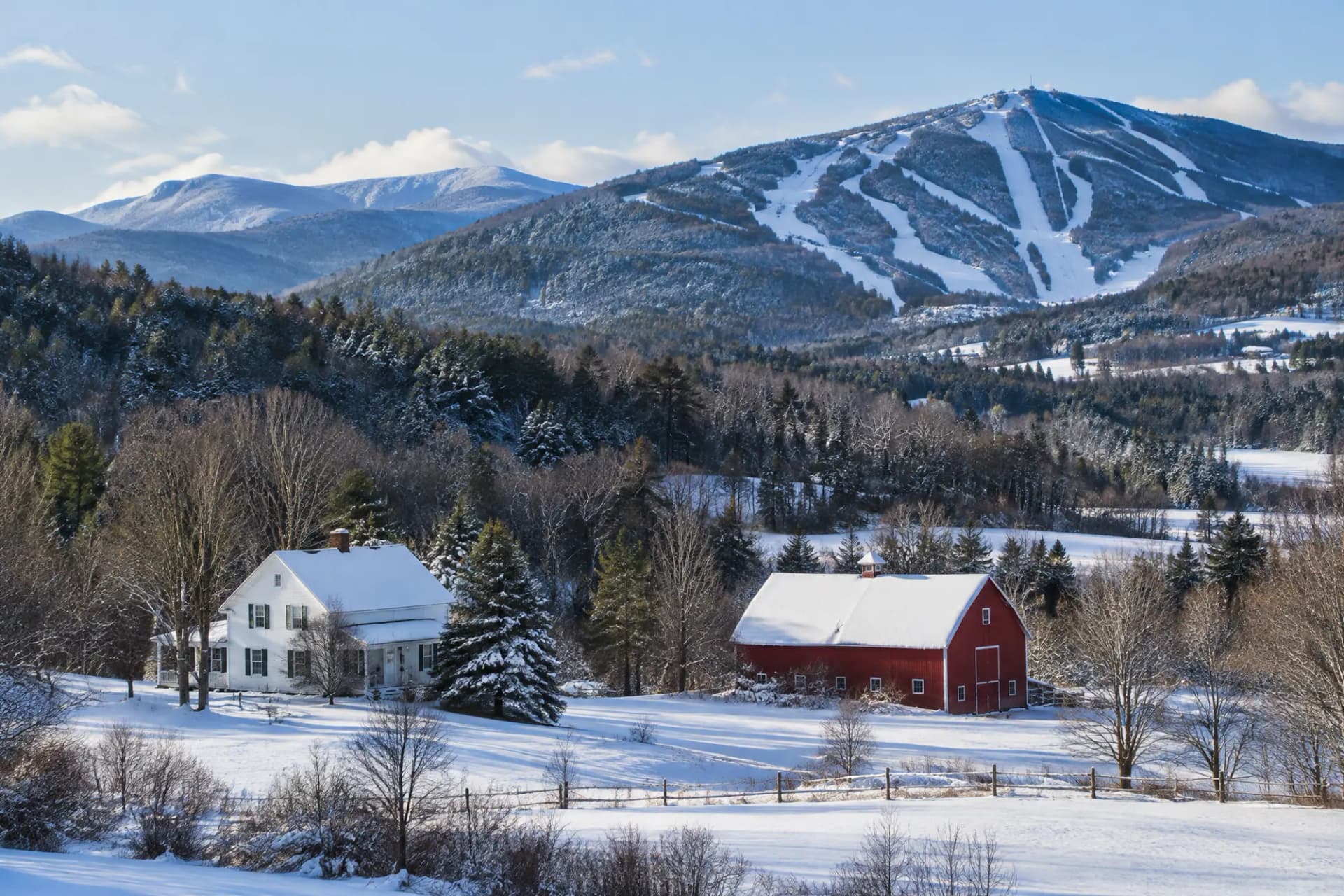 A farmhouse and red barn in a snowy New England valley